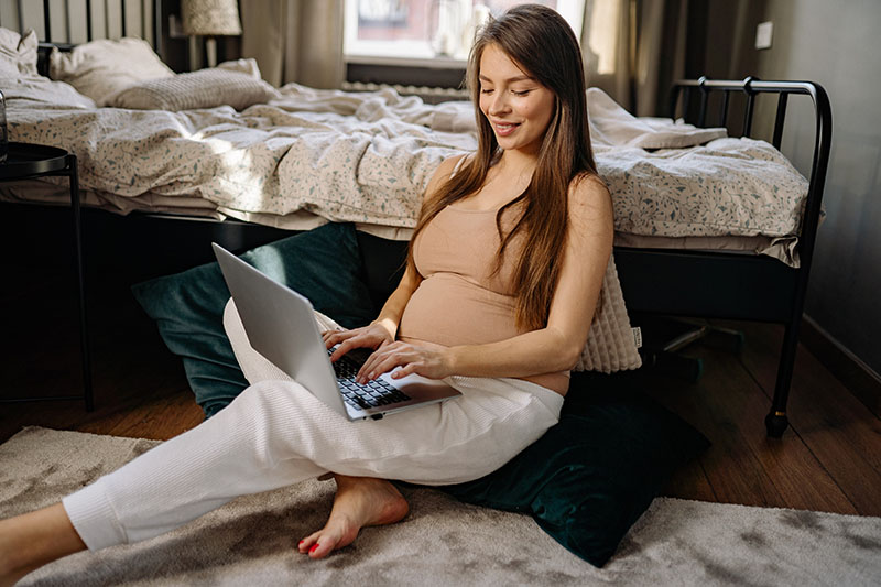 Terhes hölgy ül a földön, és dolgozik a laptopján 